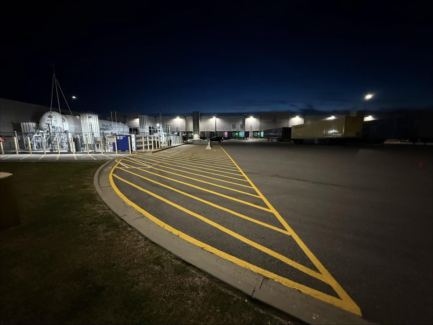 Finished yellow crosshatch markings along a curb in a distribution center truck court at night