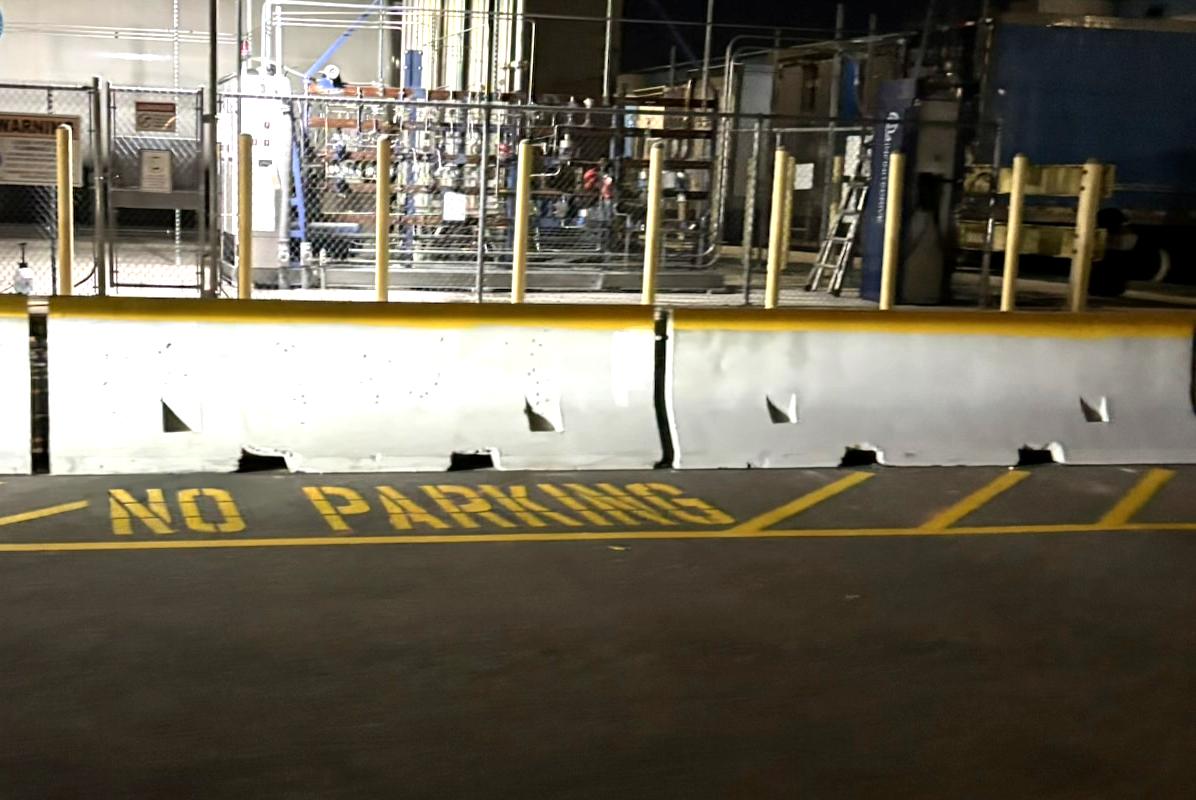 Yellow NO PARKING pavement stencil in front of concrete barriers at a distribution center