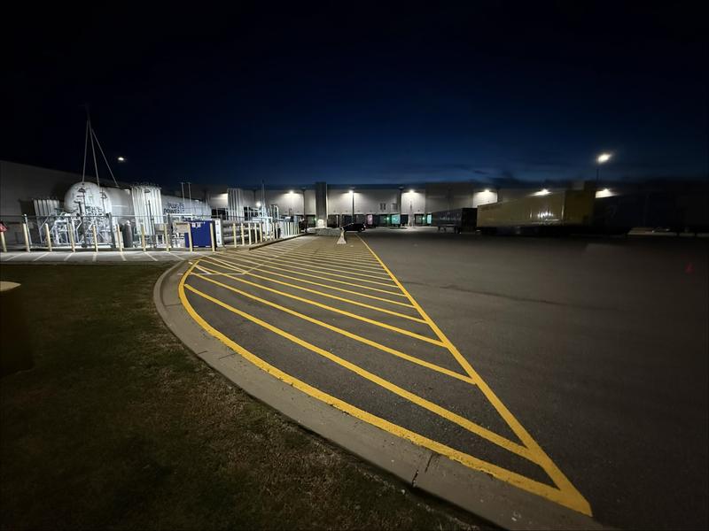 Finished yellow crosshatch markings along a curb in a distribution center truck court at night