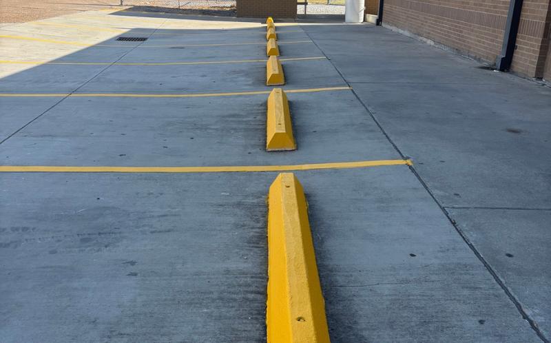 Row of concrete wheel stops freshly painted safety yellow at Kinder High School
